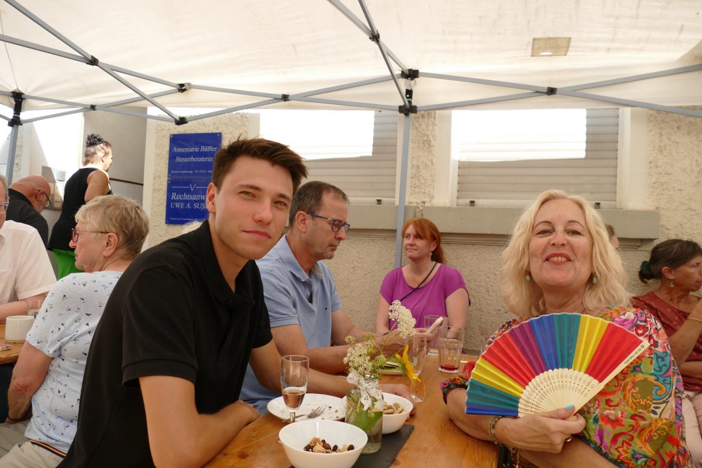 Gäste sitzen an einer Bierzeltgarnitur und unterhalten sich