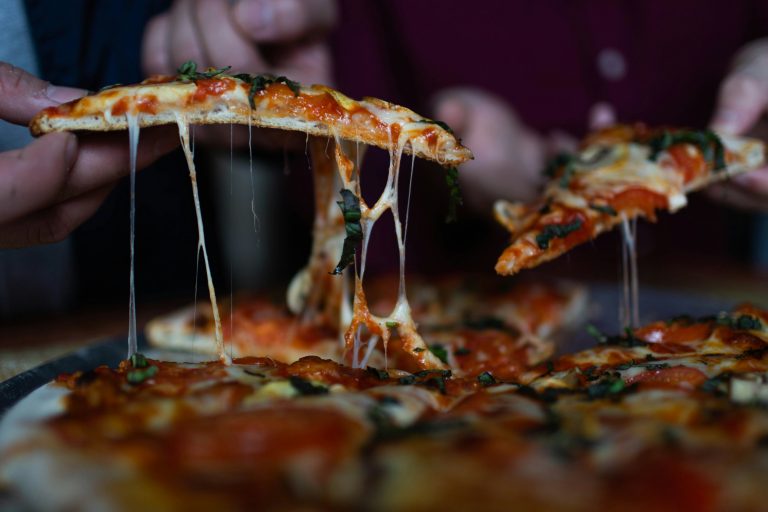 Zwei Personen nehmen ein Stück von einer Pizza.
